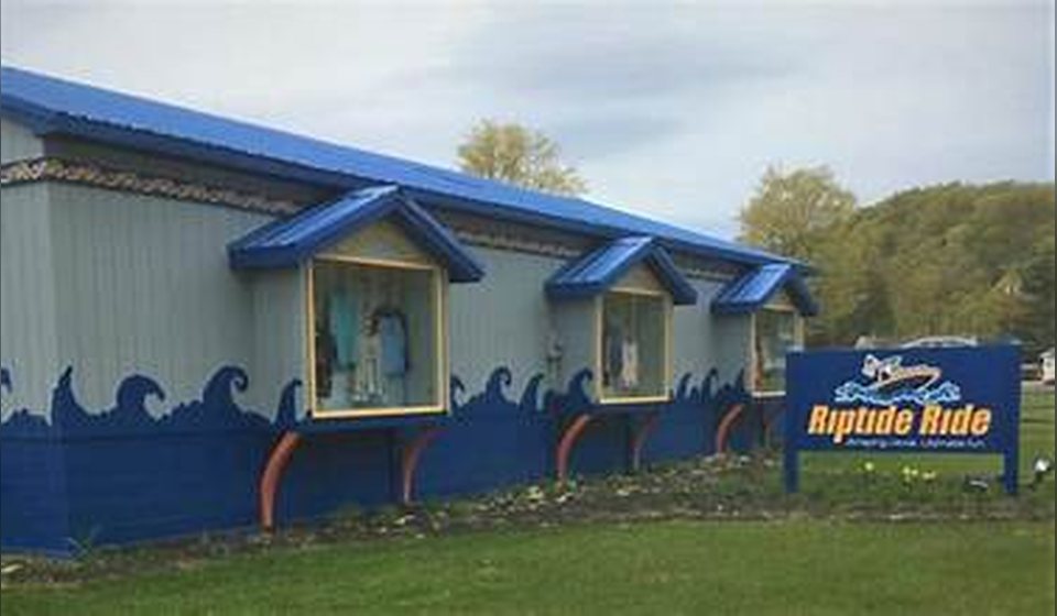 The Riptide Ride building in Munising, painted with blue waves, with its roadside sign